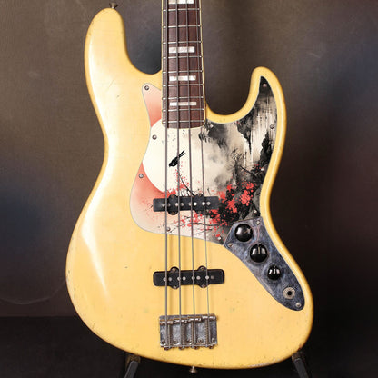 Egyedi Fender Jazz Bass gitár koptató vörös virágzó fával, ágon ülő madárral és ködös folyóparti tájképpel a háttérben