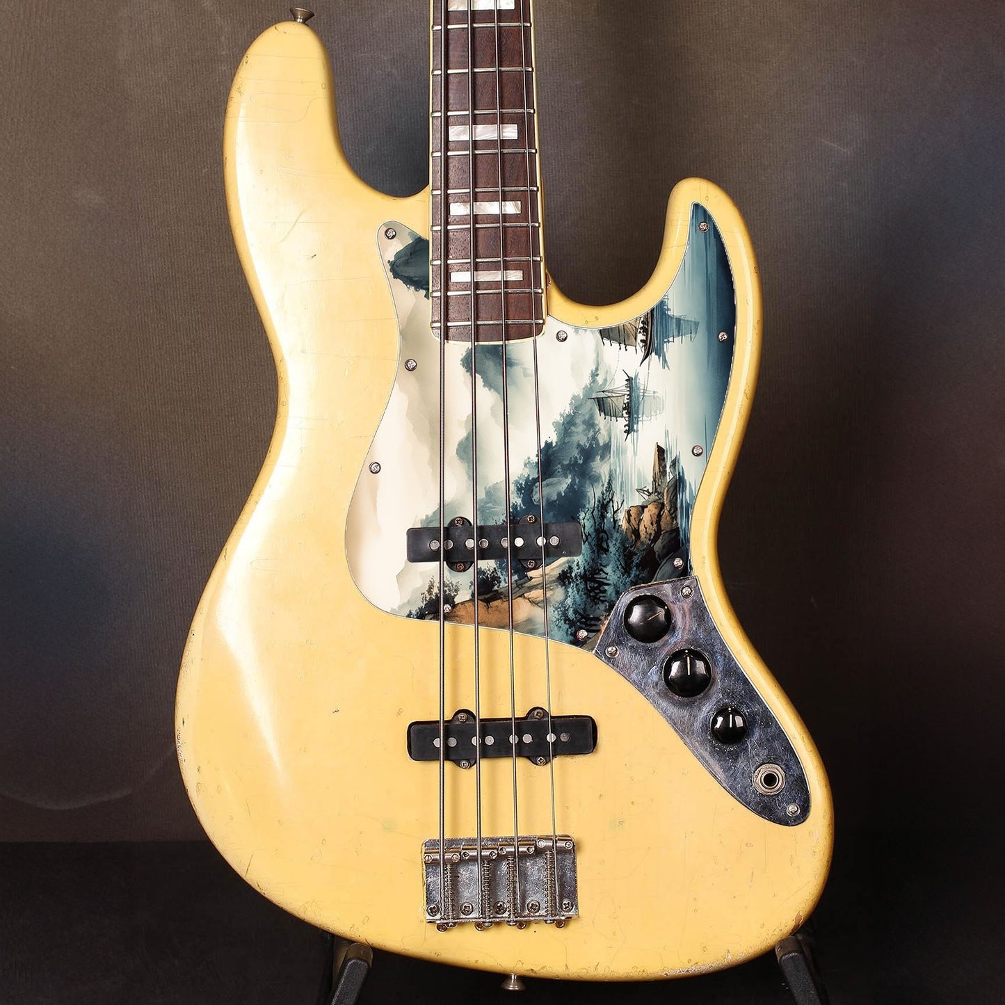 Egyedi Fender Jazz Bass gitár koptató festői tájképpel, hegyekkel, fákkal és hagyományos vitorlás hajókkal a nyugodt vízen