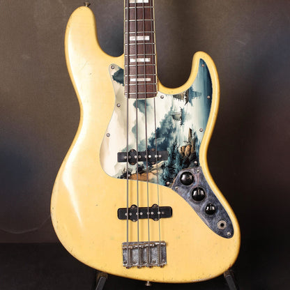 Egyedi Fender Jazz Bass gitár koptató festői tájképpel, hegyekkel, fákkal és hagyományos vitorlás hajókkal a nyugodt vízen