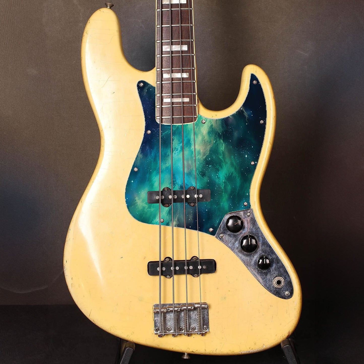 Egyedi Fender Jazz Bass gitár koptató élénk zöldes-kék galaxis mintázattal, kavargó ködfelhőkkel és szórtan ragyogó csillagokkal