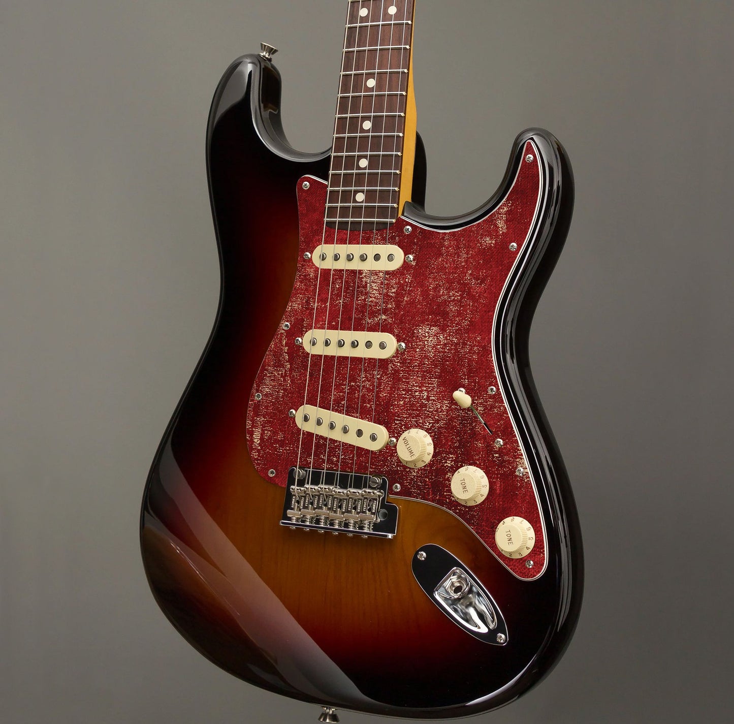 Egyedi Fender Stratocaster gitár koptató mélypiros tónusokkal, vintage hatású felülettel és rusztikus mintázattal